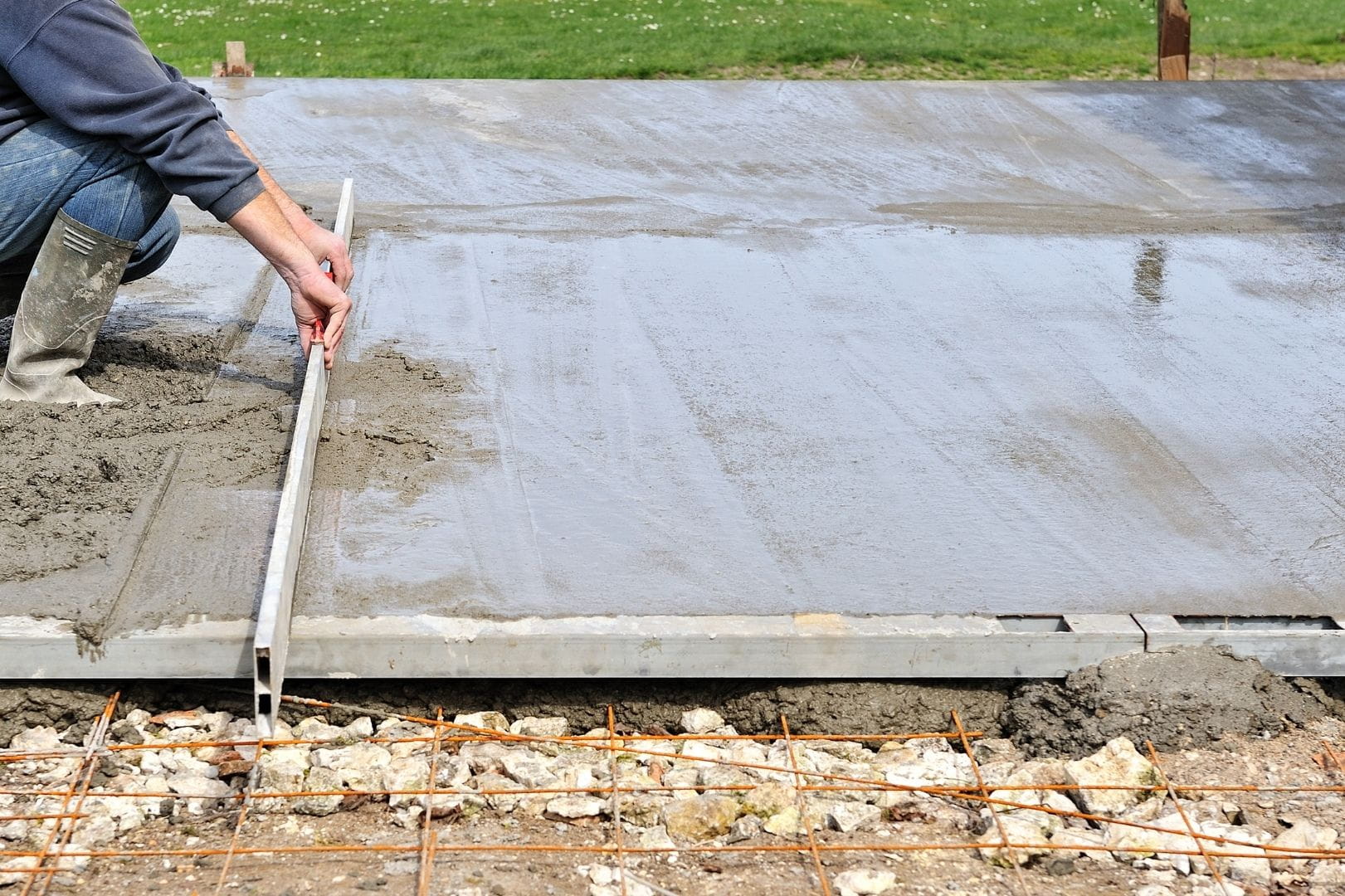 Maçon réalisant le tirage à la règle et la mise à niveau d'une dalle en béton armé sur un chantier de gros œuvre à Dreux.
