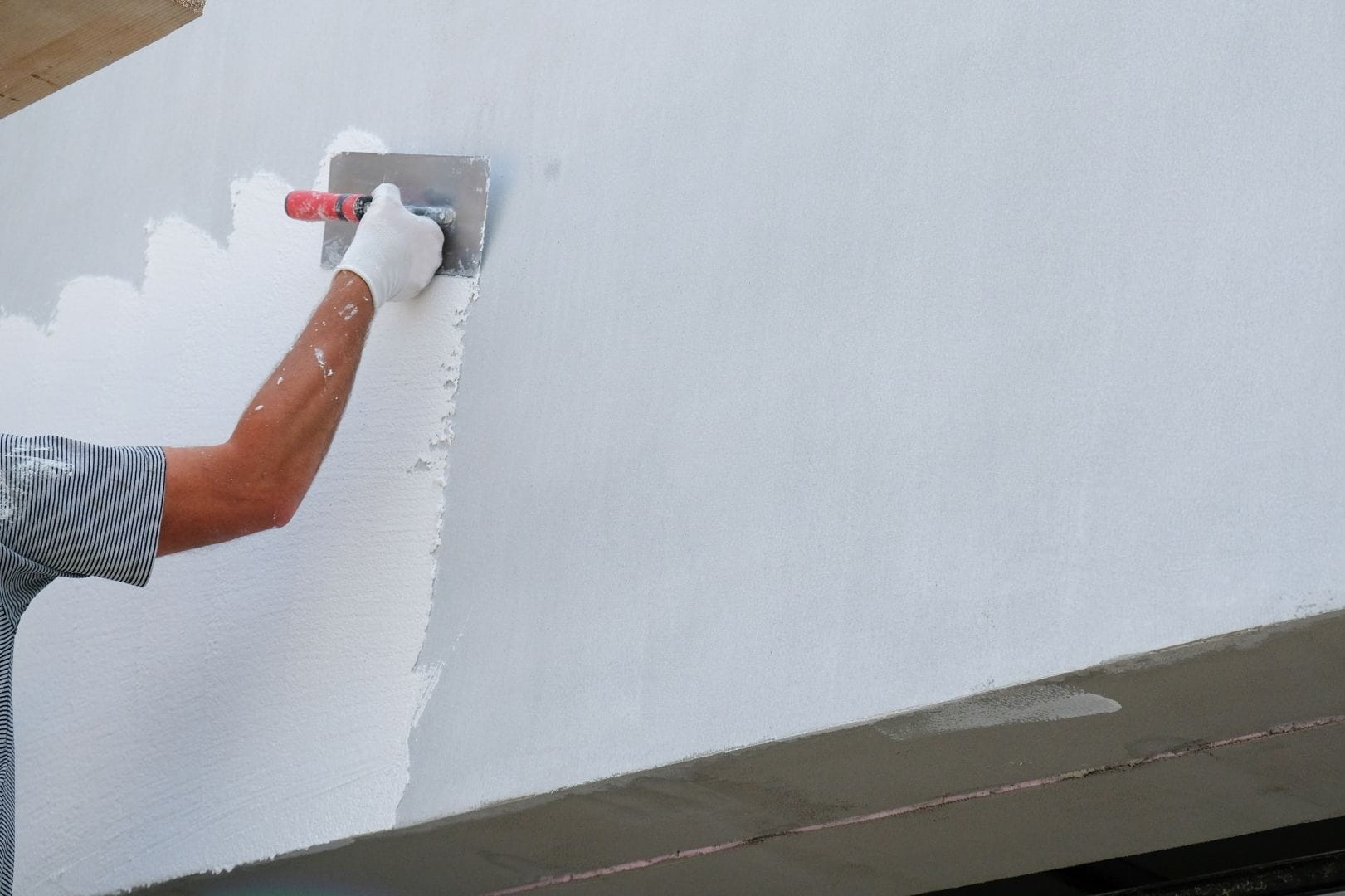 Application d'un revêtement de protection blanc à la spatule sur une paroi extérieure en rénovation.