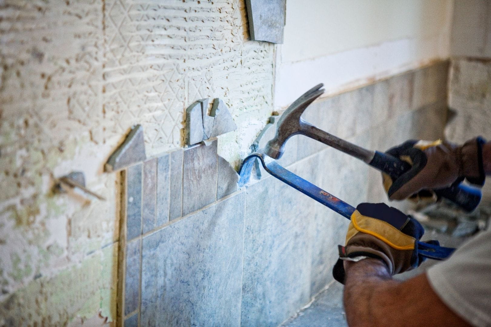 Artisan carreleur utilisant un burineur et un pied-de-biche pour la dépose d'un ancien carrelage mural.