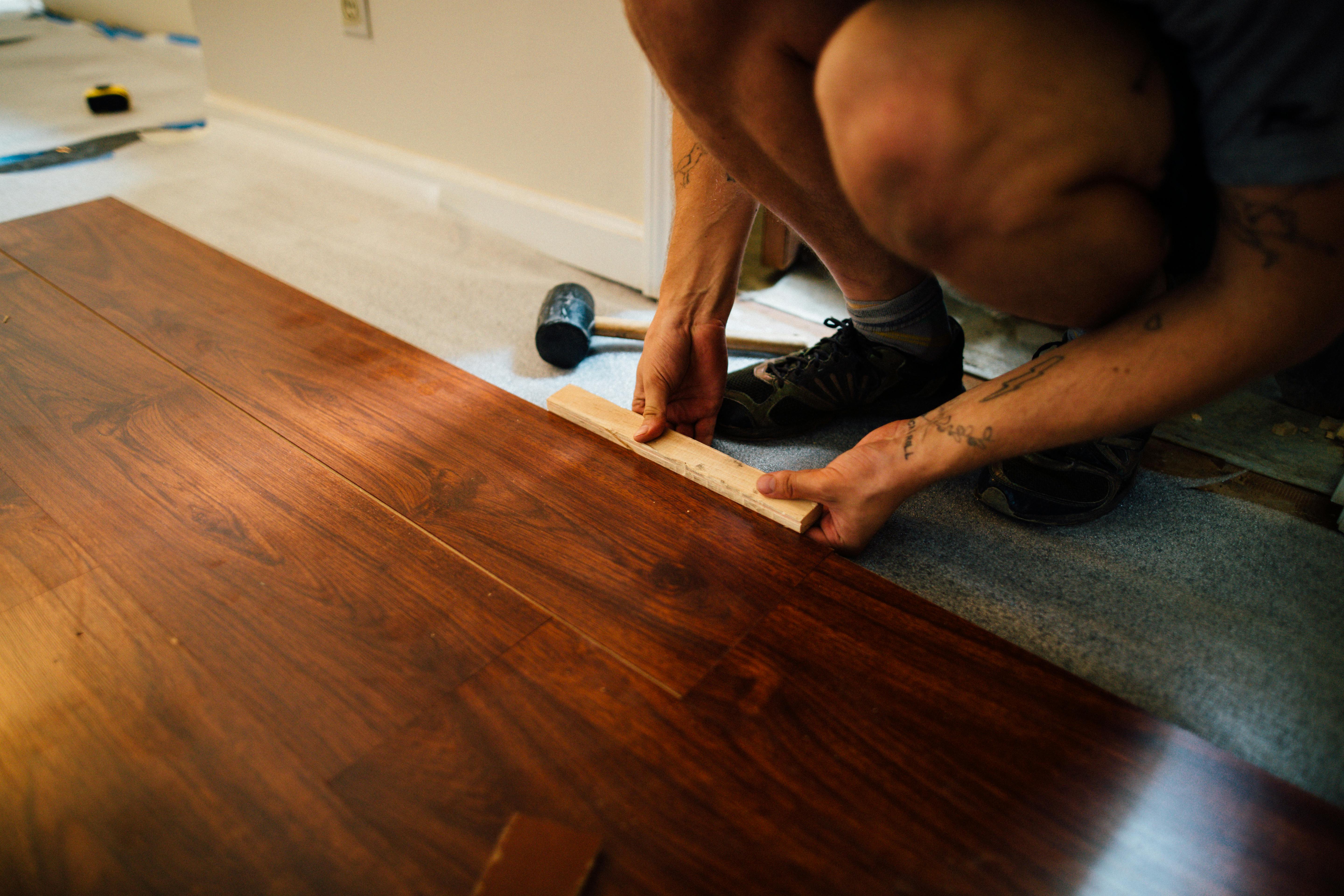 Artisan parqueteur ajustant une lame de parquet en bois exotique à l'aide d'un maillet et d'une cale.