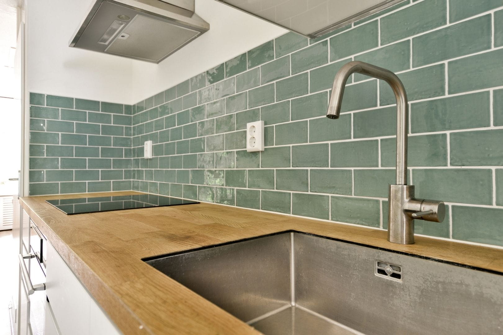 Crédence de cuisine en carrelage métro vert posée au-dessus d'un plan de travail en bois avec évier inox.